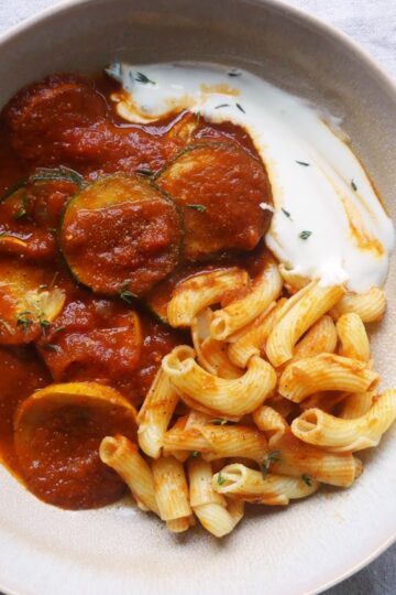 eine schale mit gebratenen zucchinischeiben in paprikasauce mit joghurt und nudeln