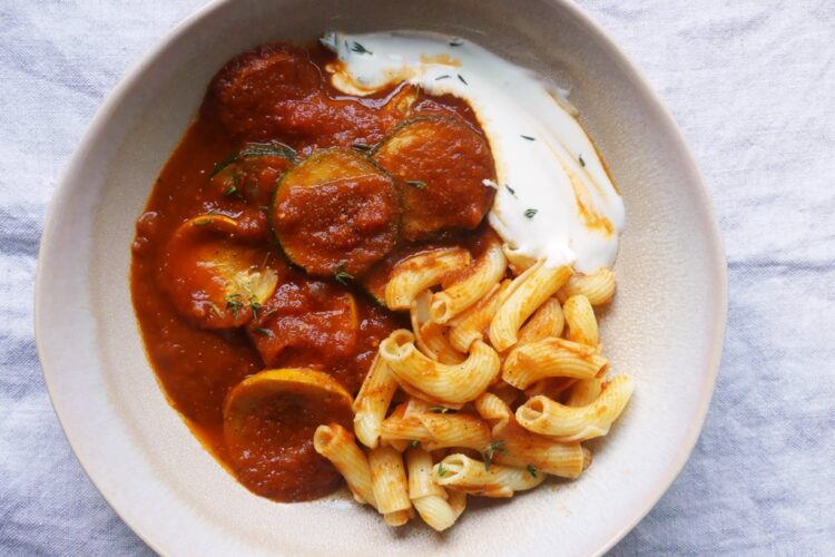eine schale mit gebratenen zucchinischeiben in paprikasauce mit joghurt und nudeln